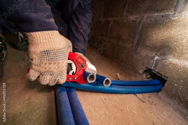 Obraz a hand cuts through a plastic heating pipe, with special scissors in gloves on the concrete floor
