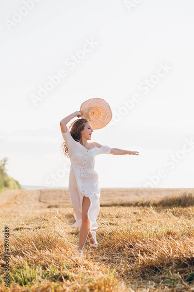 Fototapeta Girl with long curly hair poses in a wheat field
