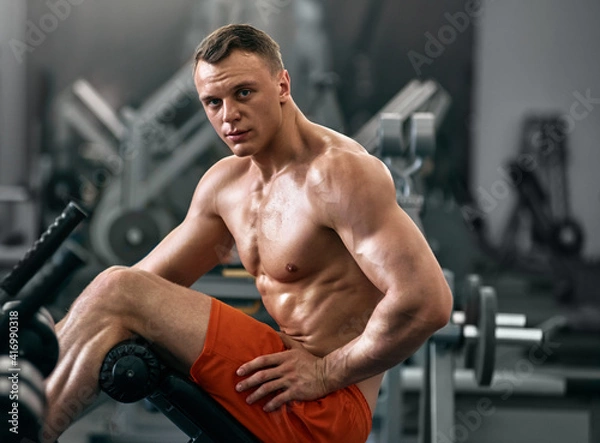 Fototapeta Portrait of young handsome smiling muscular athlete resting in gym