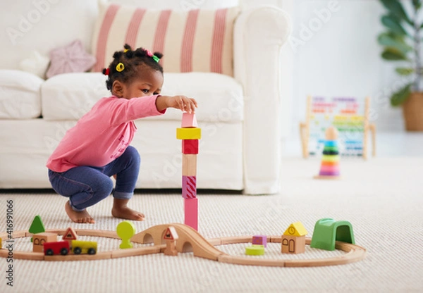 Obraz cute african american toddler baby girl playing wooden toys, stacking the tower blocks on the carpet at home