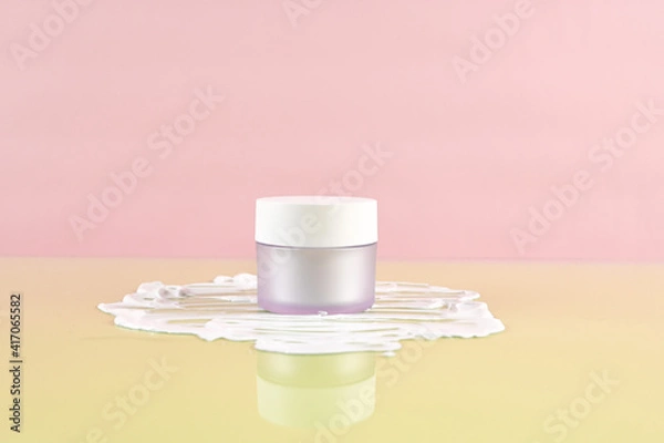 Fototapeta Moisturizer facial or eye cream in white frosted glass jar. Empty cosmetic jar on the background of the cream texture. Pastel background with copy space