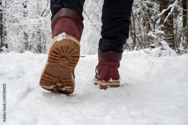 Obraz A man in boots is walking through the winter forest. Bottom view of shoes, selective focus. Concept of hikes walks and winter holidays
