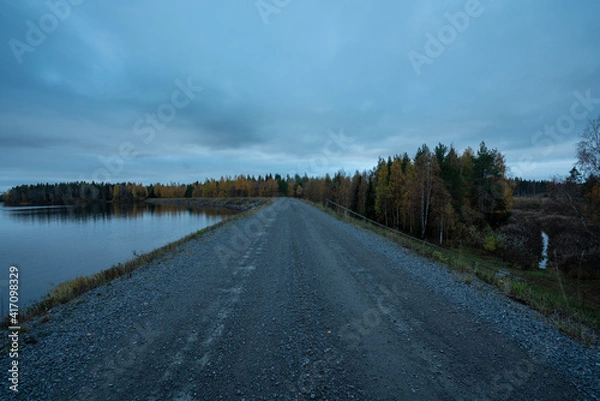 Fototapeta Man made lake with dike as road with boreal forest and low vegitation in autumn