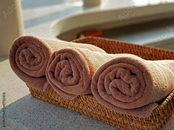 Obraz Rolled up brown bath towels in straw basket on counter outdoor.