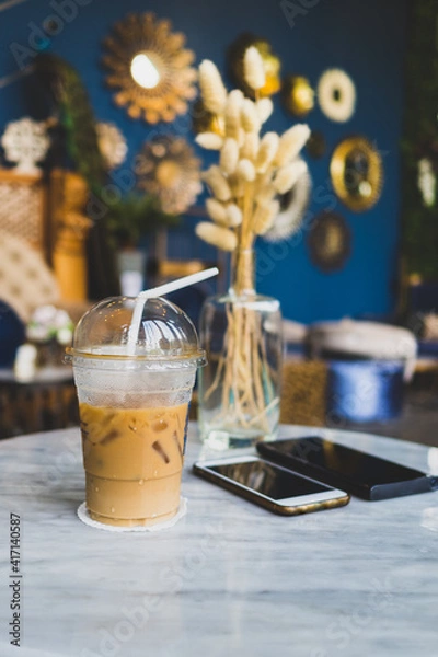 Obraz Iced coffee with straw on the white marble table with mobile phones and vase of decoration plant.