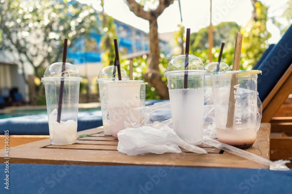 Obraz Used empty plastic cups with straws on wooden table near sun bed. Beverages delivery concept.