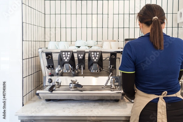 Obraz Female Barista in protective mask is standing and making coffee by using coffee machine at cafe.
