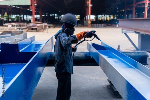 Fototapeta The painter is working to painting color top coat on steel structure with spray gun, at industrial factory.