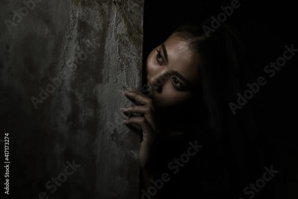 Obraz Scared woman hiding behind wall in dark room Young crazy scared and shocked asian woman escape murderer and get frightened Copy space Facial expression, human emotion concept Looking horror Halloween