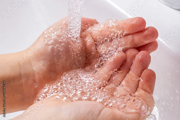 Fototapeta Children's hands under the running water from the faucet in the bathroom.