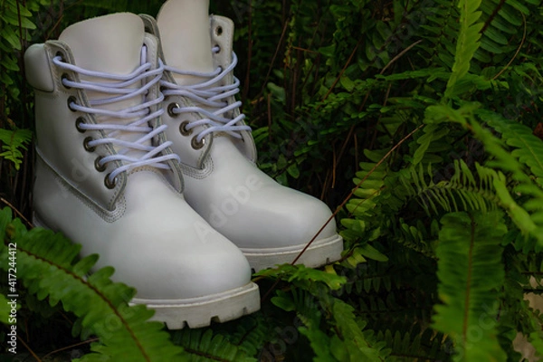 Fototapeta Close-up of a pair of all-white boots, with a low platform sole, surrounded by green vegetation