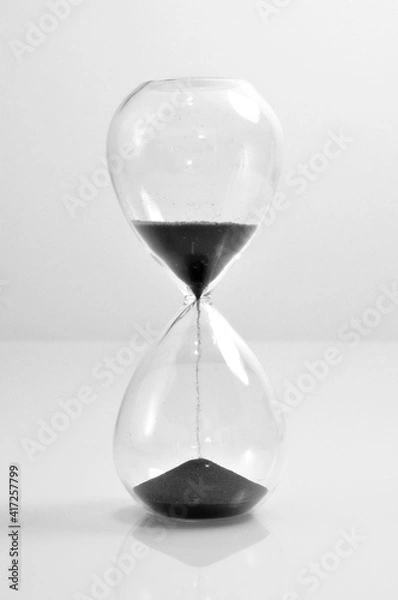 Obraz Hourglass transparent crystal black sand falling down vertical old vintage clock isolated on white background 