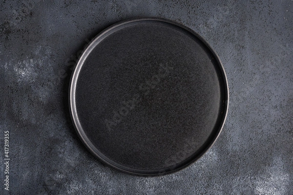 Fototapeta Empty round black plate on dark moody dark background with copy space. Overhead view