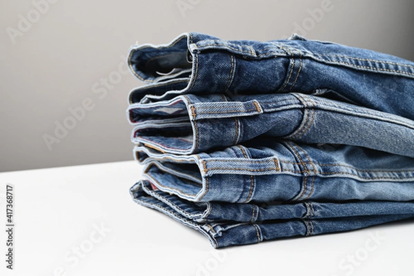 Fototapeta A set of folded jeans on white table, side view. Wardrobe in the casual style. Collection of jeans.