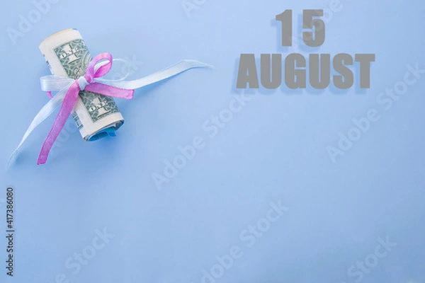 Fototapeta calendar date on blue background with rolled up dollar bills pinned by blue and pink ribbon with copy space. August 15 is the fifteenth day of the month