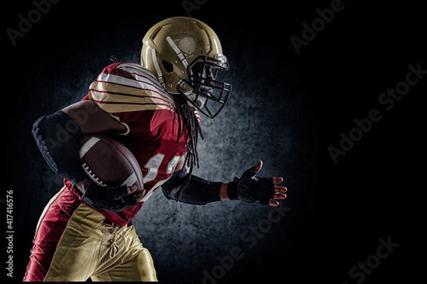 Fototapeta American football player. Sportsman with ball in helmet on stadium in action.