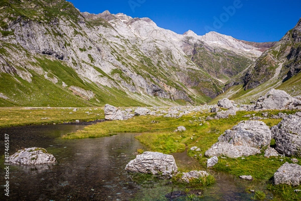 Obraz Lake surrounded by grass, rocks and high mountains in summertime
