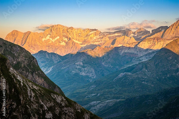 Obraz Beautiful sunset over the mountains, with the sun illuminating the high peaks and the valley remaining in shadow