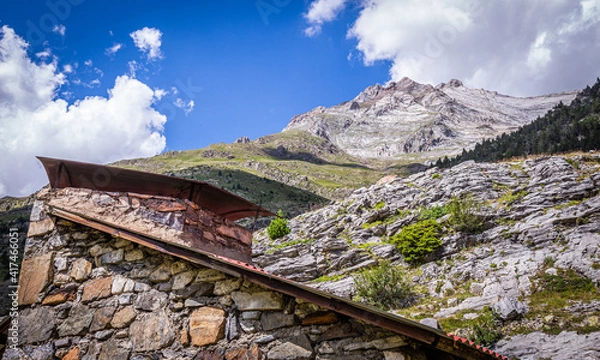 Obraz Beautiful view of a mountain top from a hut with a chimney in a green meadow in summertime