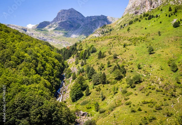 Obraz Beautiful spring landscape with green meadows, forests, a river and mountains in the background, under a blue sky