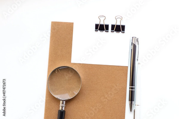 Fototapeta White office desk with magnifying glass, notepad with sticky note, pen with copy space. Accounting work space