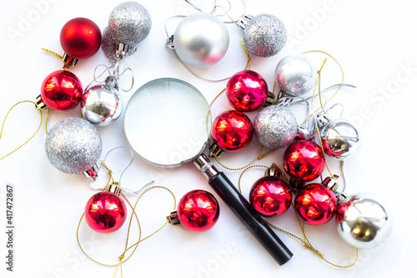 Fototapeta Magnifier glass on white table whith red and silver decoration ball. Business concept in new year. Search idea