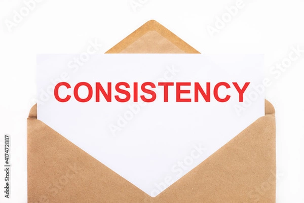 Fototapeta A white sheet with the text consistency lies in an open craft envelope on a white background with copy space. Business concept image