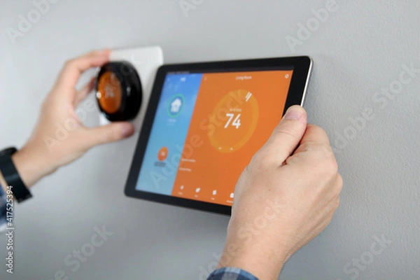 Fototapeta Man is Adjusting a  temperature using a tablet with a smart home app in modern living room