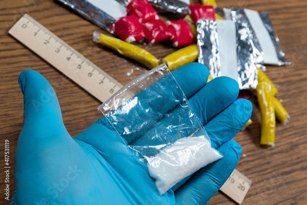 Fototapeta evidence of smuggling traffic: Packaging of a narcotic substance in the hand of a forensic expert against the background of other arrested materials, cocaine, heroin, spice