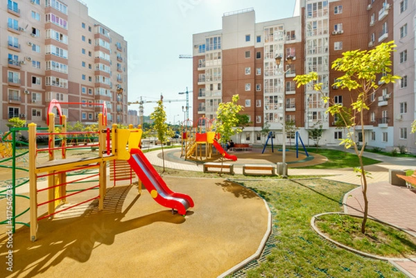 Fototapeta New modern colorful children playground in sunny summer green courtyard among residential high-rise buildings