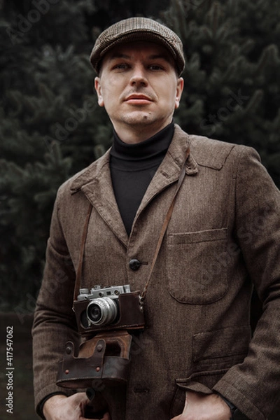 Obraz photographer with a retro camera in his hands. Dressed in retro style, jacket and cap