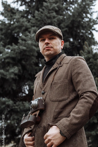 Obraz photographer with a retro camera in his hands. Dressed in retro style, jacket and cap