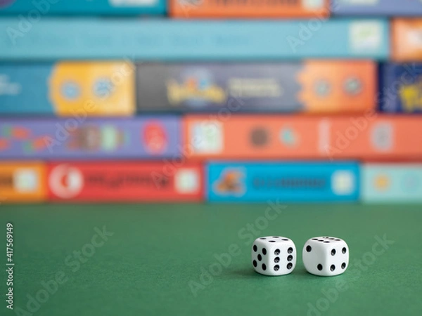 Fototapeta Two dice on the background of board game boxes. Dice games for kids, tweens and adults