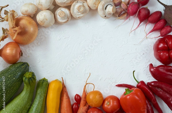 Fototapeta Frame of various vegetarian ingredients ready for cooking on the white table. Organic healthy food: colorful vegetables on the white background. Top view with copy space for text