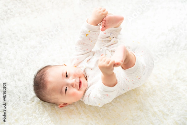 Obraz 足を持って笑顔で寝転んでいる赤ちゃん