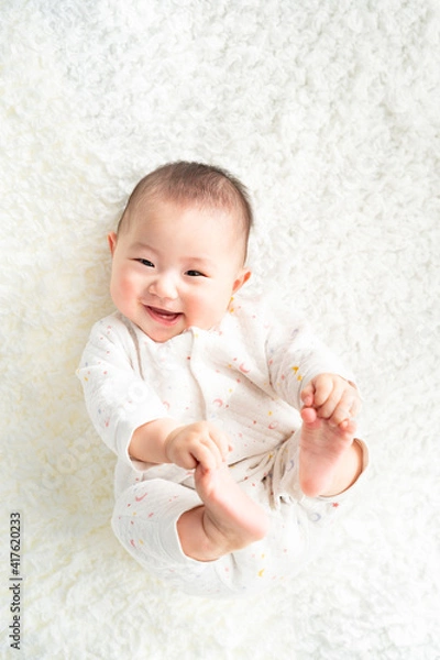 Obraz 足を持って笑顔で寝転んでいる赤ちゃん