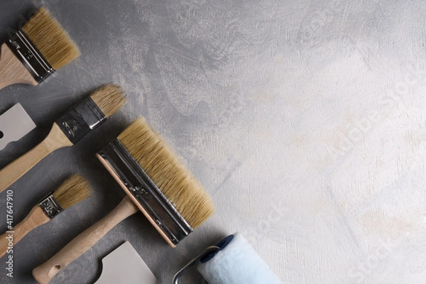 Fototapeta Spatulas for application of putty and brushes and rollers for painting on a gray concrete background.Top view