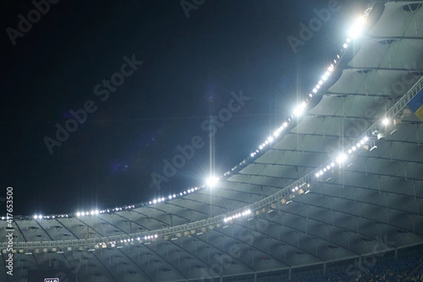 Fototapeta Stadium lit floodlighting into the darkness of the evening. Bokeh effect.