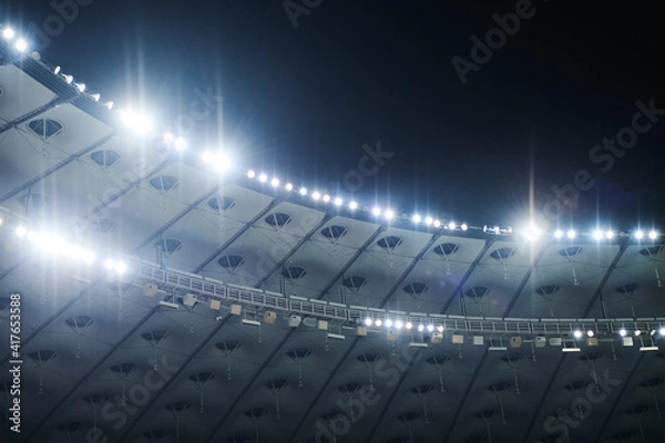 Fototapeta Stadium lit floodlighting into the darkness of the evening. Bokeh effect.