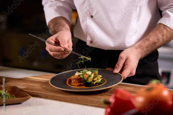 Fototapeta chef dressing salad with fresh greens, adding finishing touch on dish before it is going to be served for restaurant guests