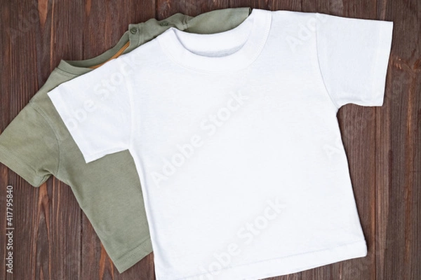 Fototapeta White tshirt mockup on brown wooden background. Template, flat lay. Clothes mockup, kid shirt