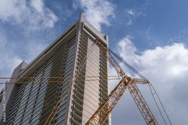 Fototapeta Tall building with crane in front and blue sky background