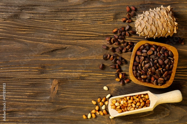 Obraz Pine nuts and pine cone on wooden background, place for text
