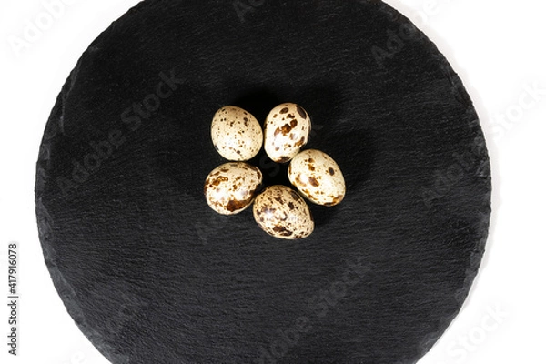 Obraz Boiled spotted quail eggs  on black stone plate , isolated on white background. Healthy Food Products Concept.