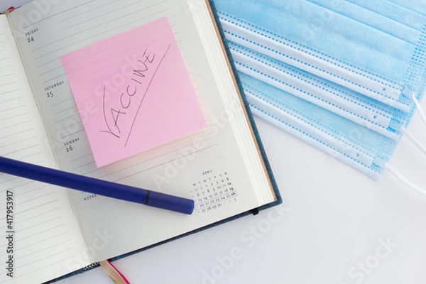 Fototapeta Concept of planning vaccination in 2021. Closeup of an open planner with marked date of the vaccination and protective face masks.