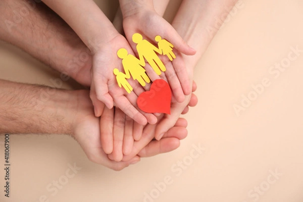 Fototapeta Parents and kid holding paper cutout of family with heart in hands on beige background, top view
