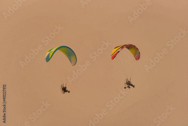 Fototapeta Silhouette of the Paramotor gliding and flying In the air through soft sunlight sky