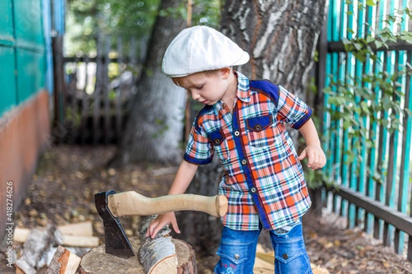 Fototapeta the child cuts wood with an axe and throws it into a pile