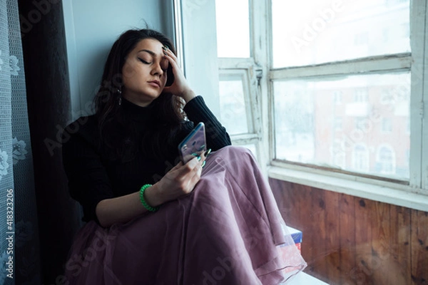 Fototapeta a depressed girl sits at the window and talking on the phone