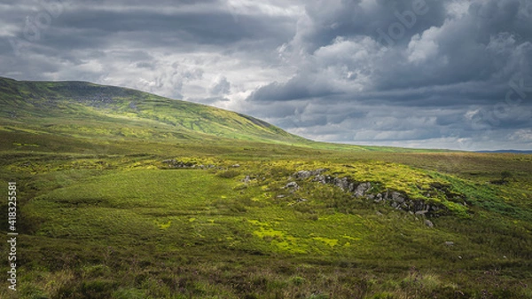 Fototapeta Green hills and fields illuminated by sunlight in Cuilcagh Mountain Park with dramatic stormy sky, Northern Ireland